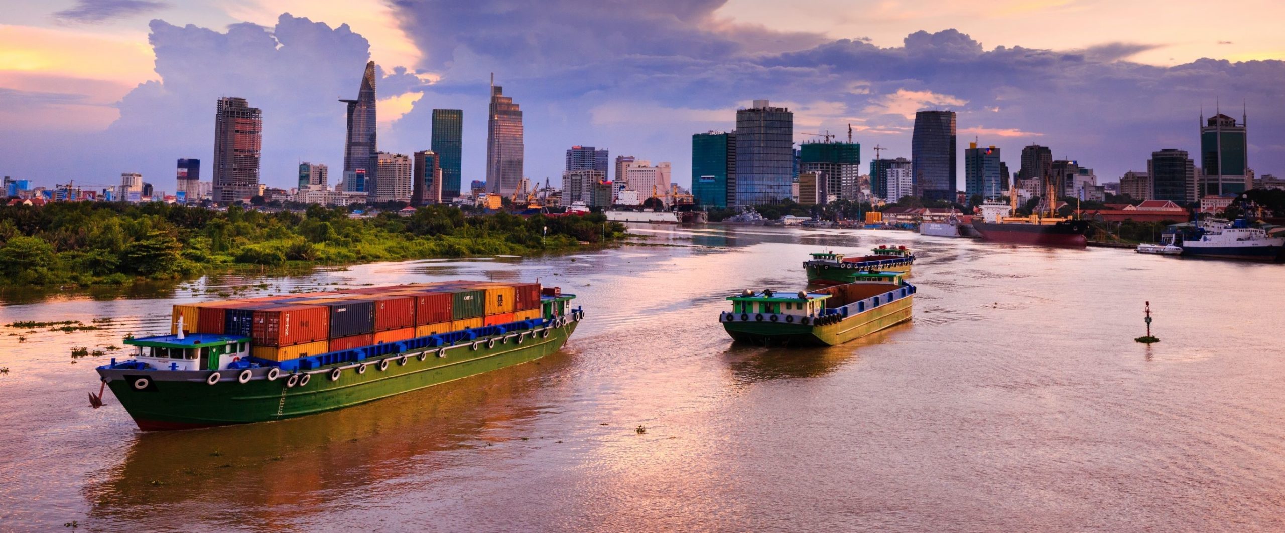 Container barges travelling along a river beside a city skyline